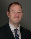 a man wearing a suit and tie smiling and looking at the camera
